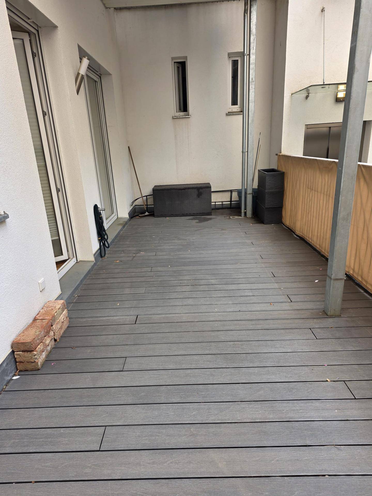 Große Außenterrasse mit modernen grauen Dielen und Blick auf die umliegenden Gebäude.