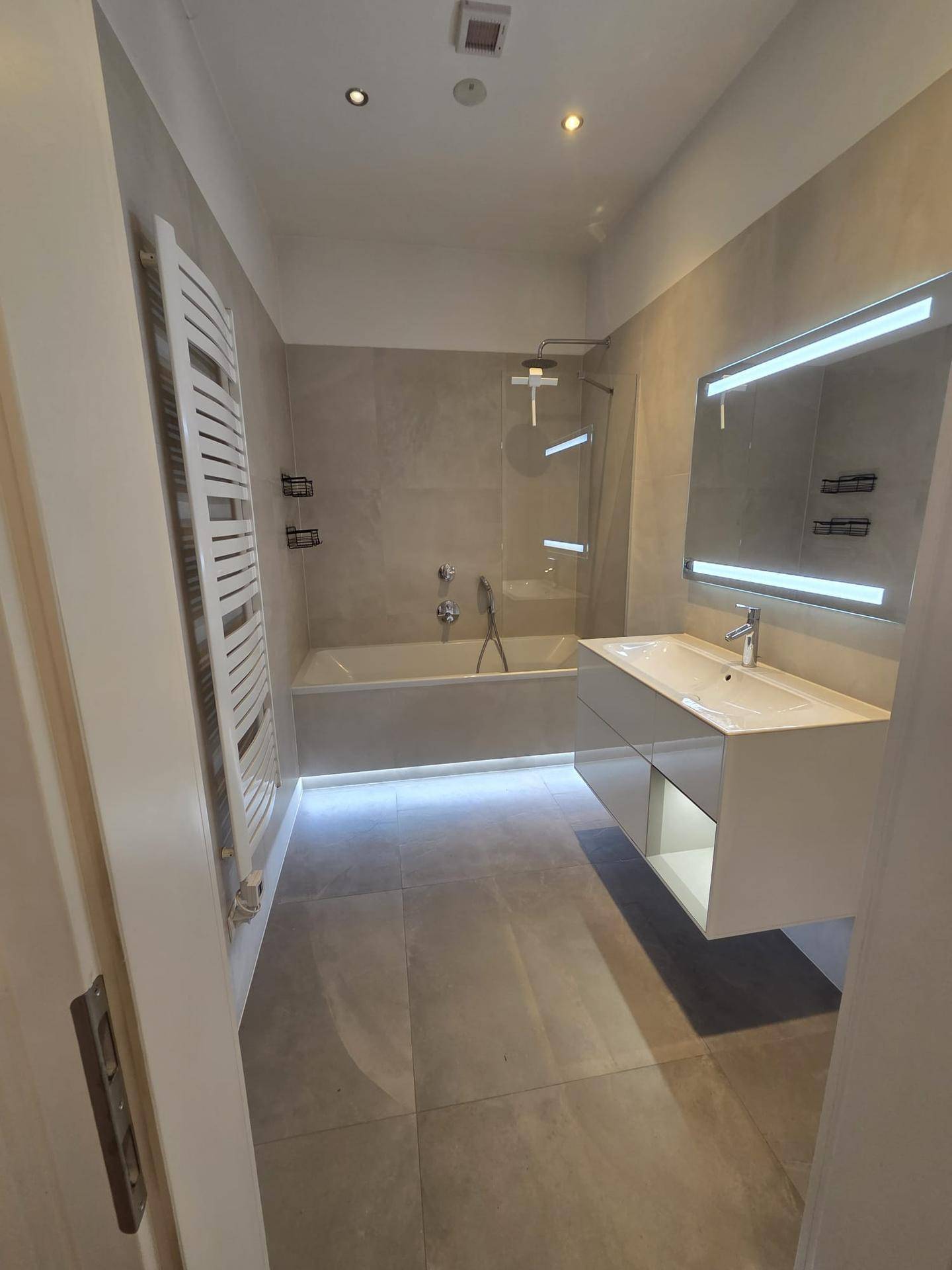 Modernes Badezimmer mit Badewanne, Duschbereich, schwebendem Waschtisch und beheiztem Handtuchhalter.