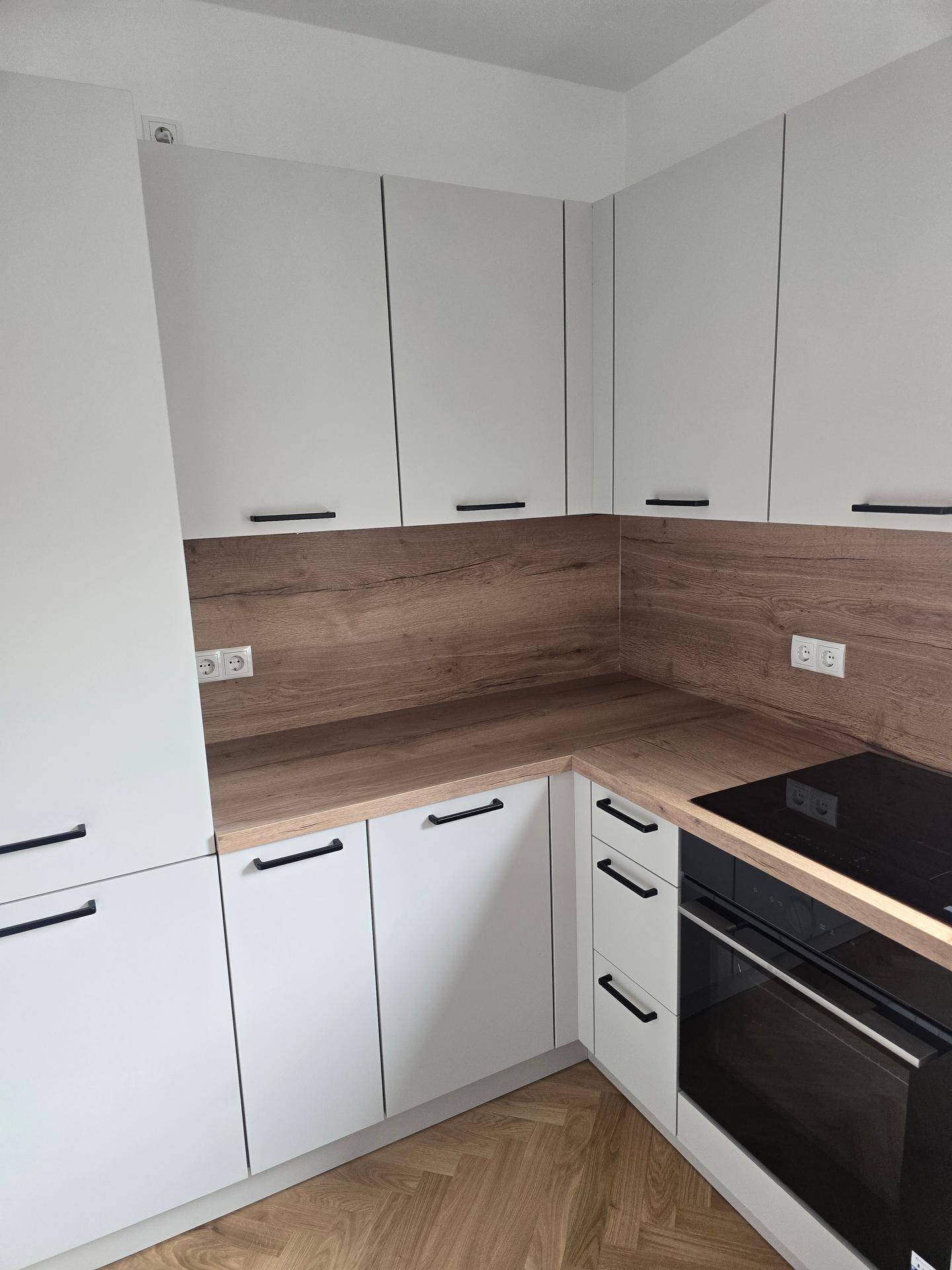 Moderne Einbauküche mit weißen Schränken, Holzoptik-Arbeitsplatte und Induktionskochfeld.