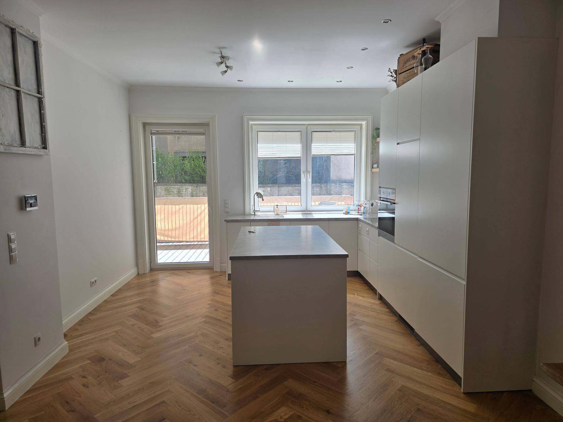 Helle, moderne Küche mit Kücheninsel, Einbaugeräten und Zugang zu einem Balkon.