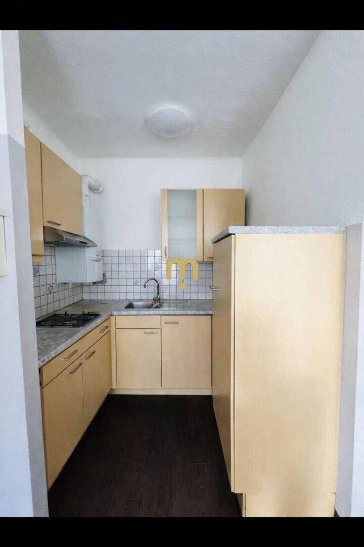 Kleine, funktionale Küchenzeile mit hellen Holzschränken, Fliesenrückwand und Gasherd.