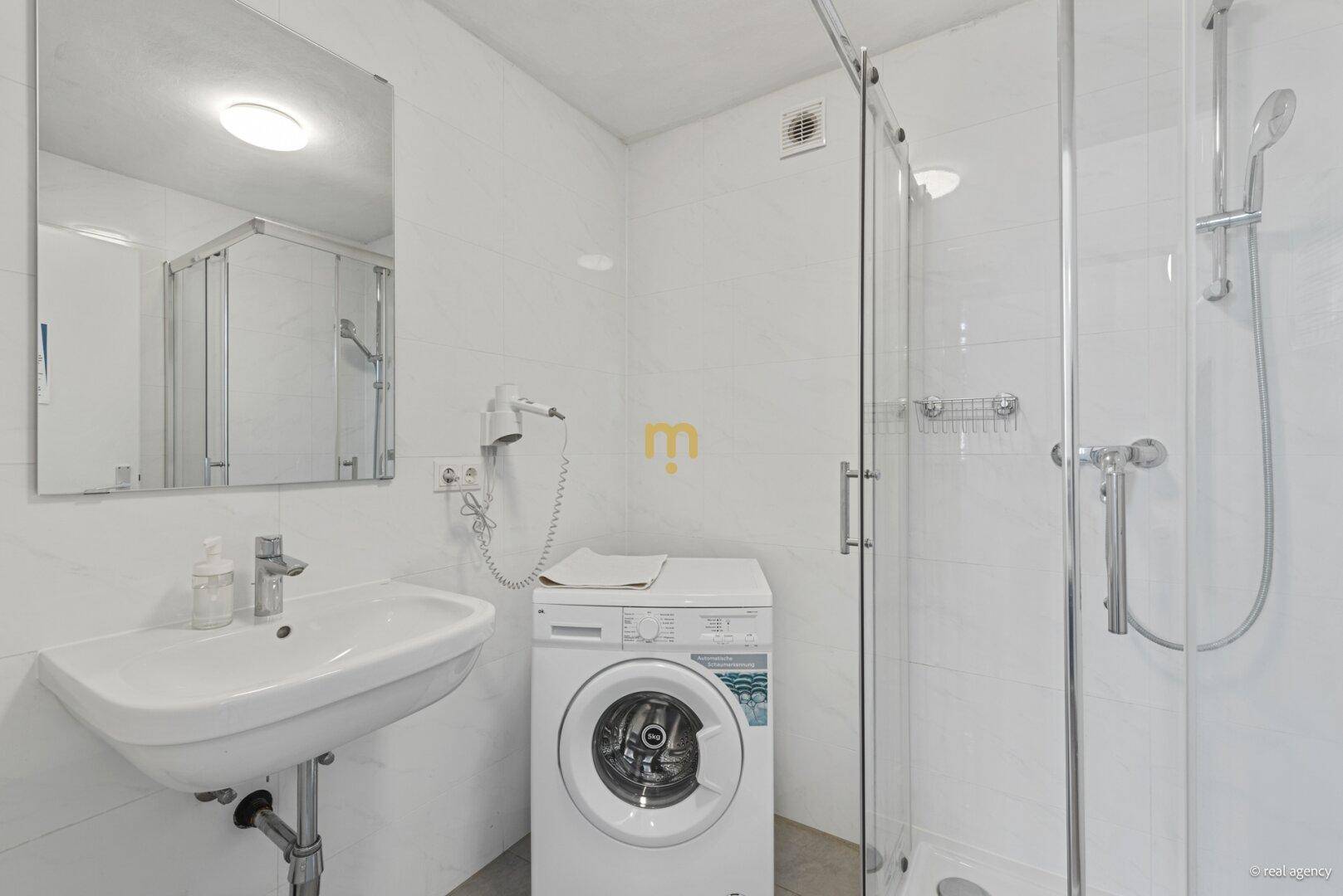 Modernes Badezimmer mit Duschkabine, Waschbecken und integrierter Waschmaschine.