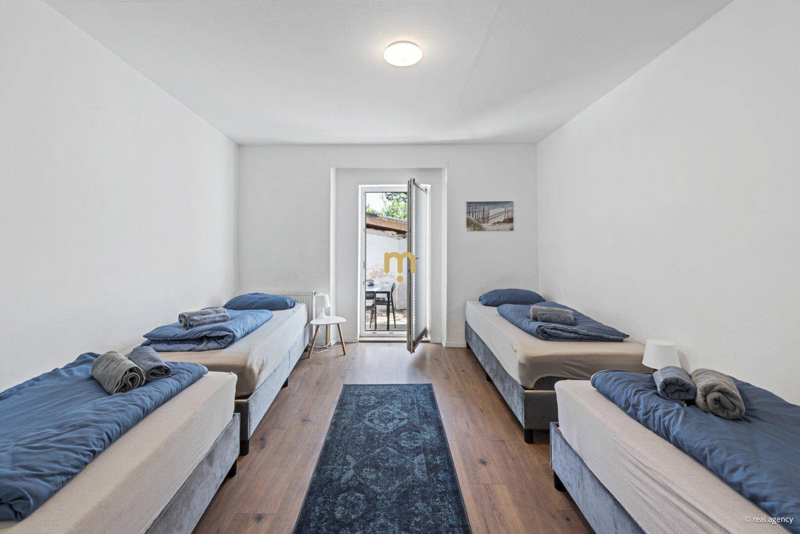 Helles Schlafzimmer mit vier Einzelbetten und direktem Zugang zu einem Außenbereich.