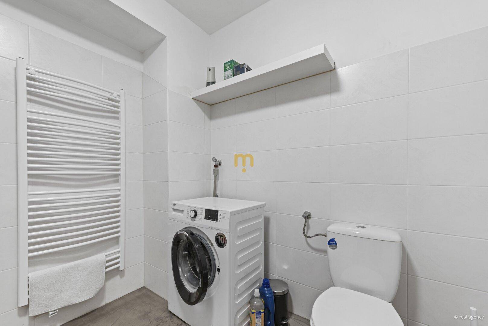 Praktischer WC-Raum mit Toilette, Waschmaschine und beheiztem Handtuchhalter.