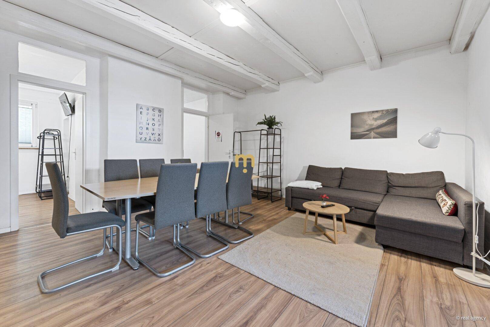 Heller Wohn-Essbereich mit modernem Sofa, großem Esstisch und sichtbaren Deckenbalken.