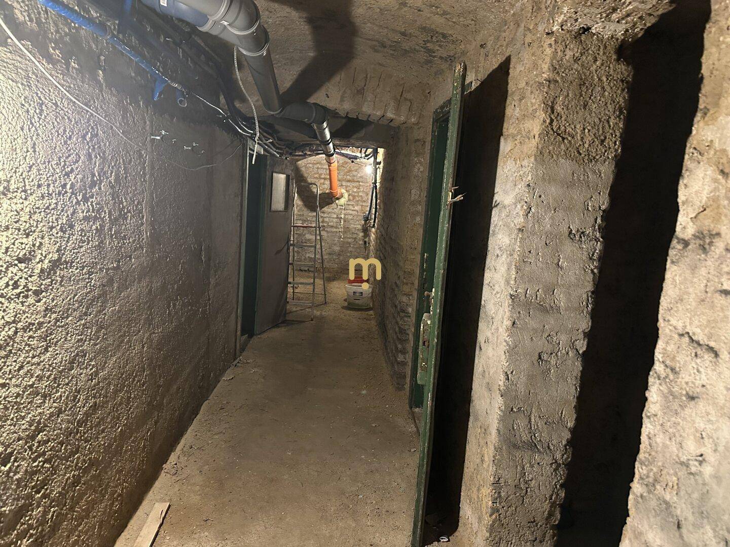 Unausgebauter Kellerflur mit sichtbaren Rohren und rauen Wänden, ideal als Stauraum.
