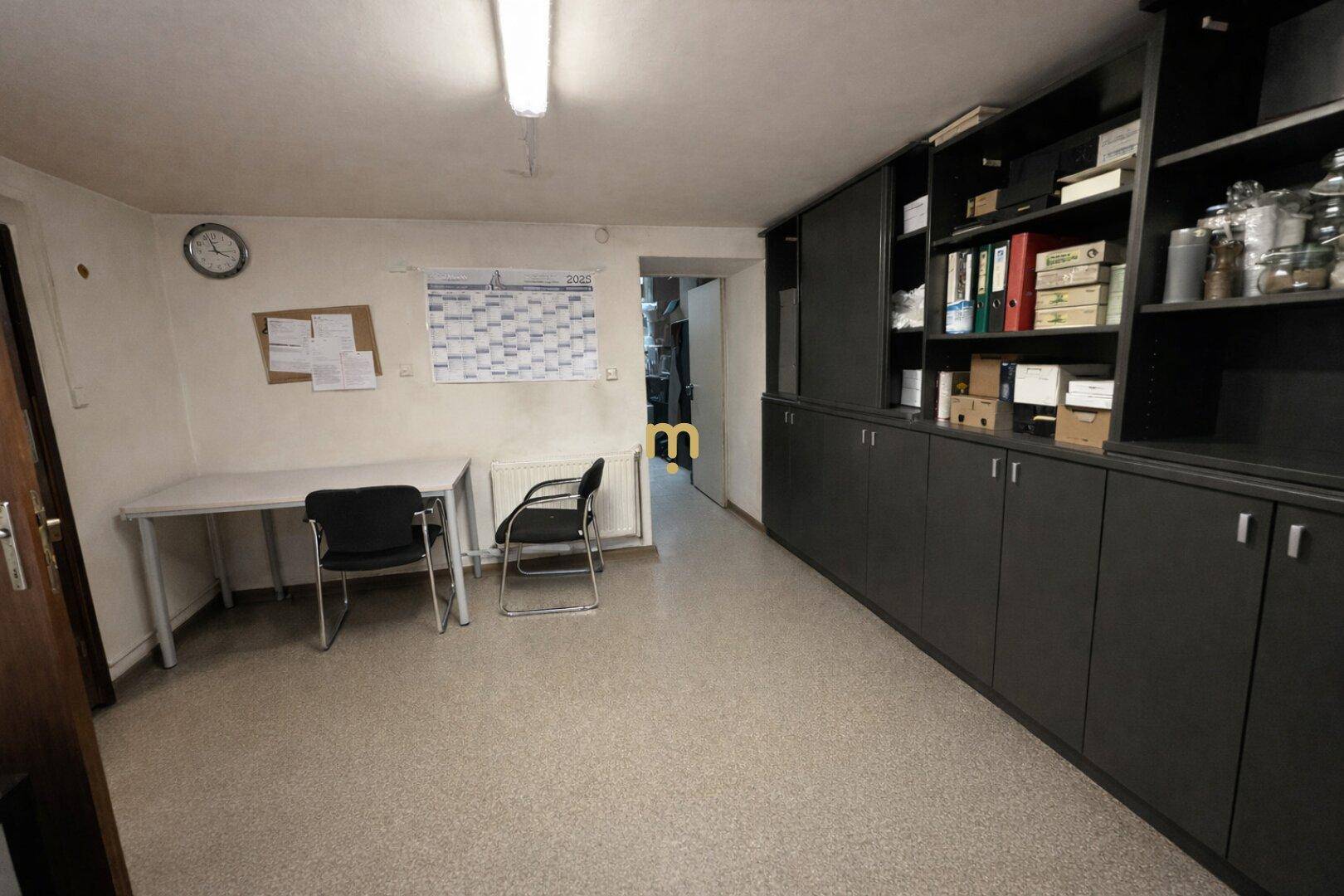 Ein kleines Büro mit Schreibtisch, Stühlen und einer langen Wand mit Einbauschränken.