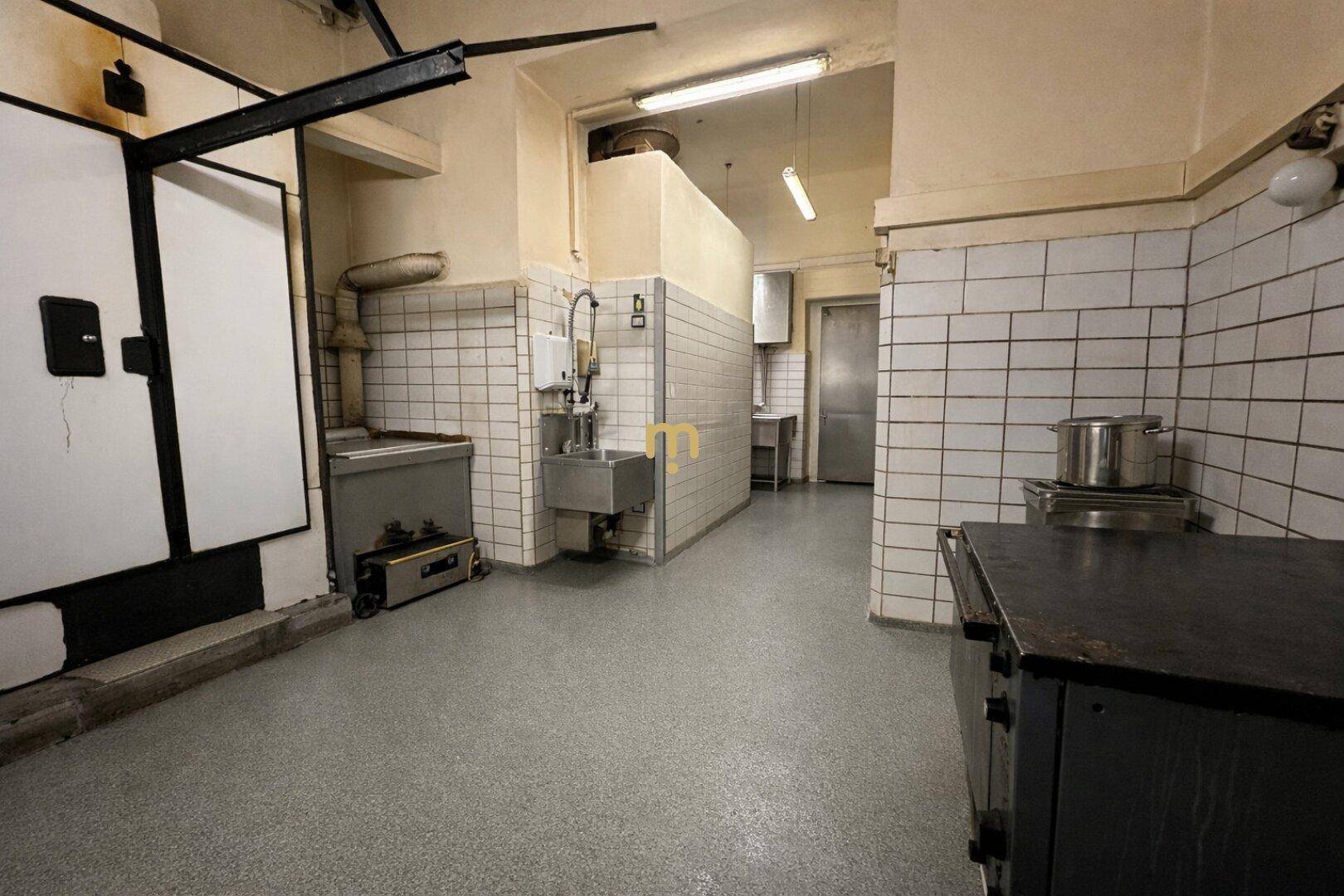 Große Industrieküche mit gefliesten Wänden, Arbeitsflächen und professionellen Geräten.