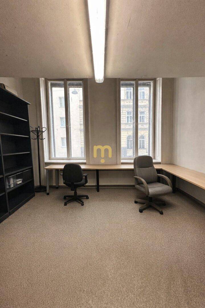 Geräumiges Büro mit zwei großen Fenstern, Schreibtischen und einem Bürostuhl.