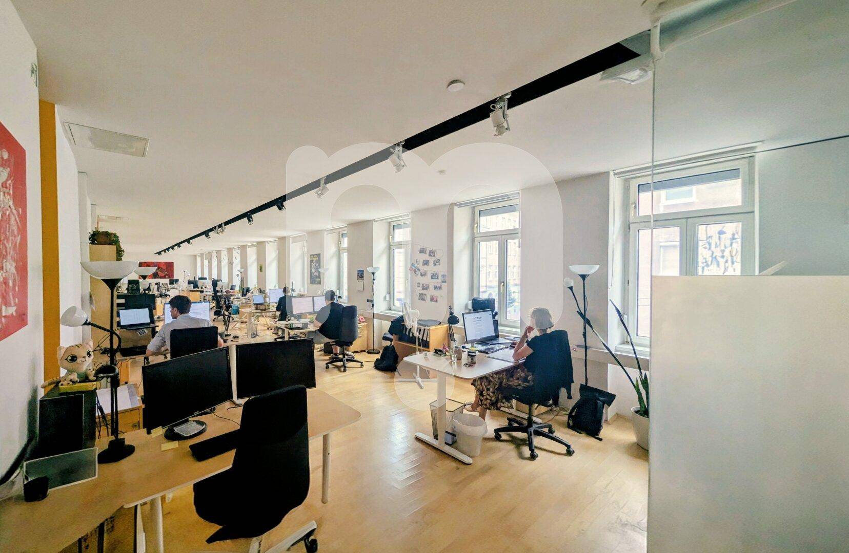 Großraumbüro mit vielen Arbeitsplätzen, Computern und natürlichem Licht durch die Fenster, modern eingerichtet.