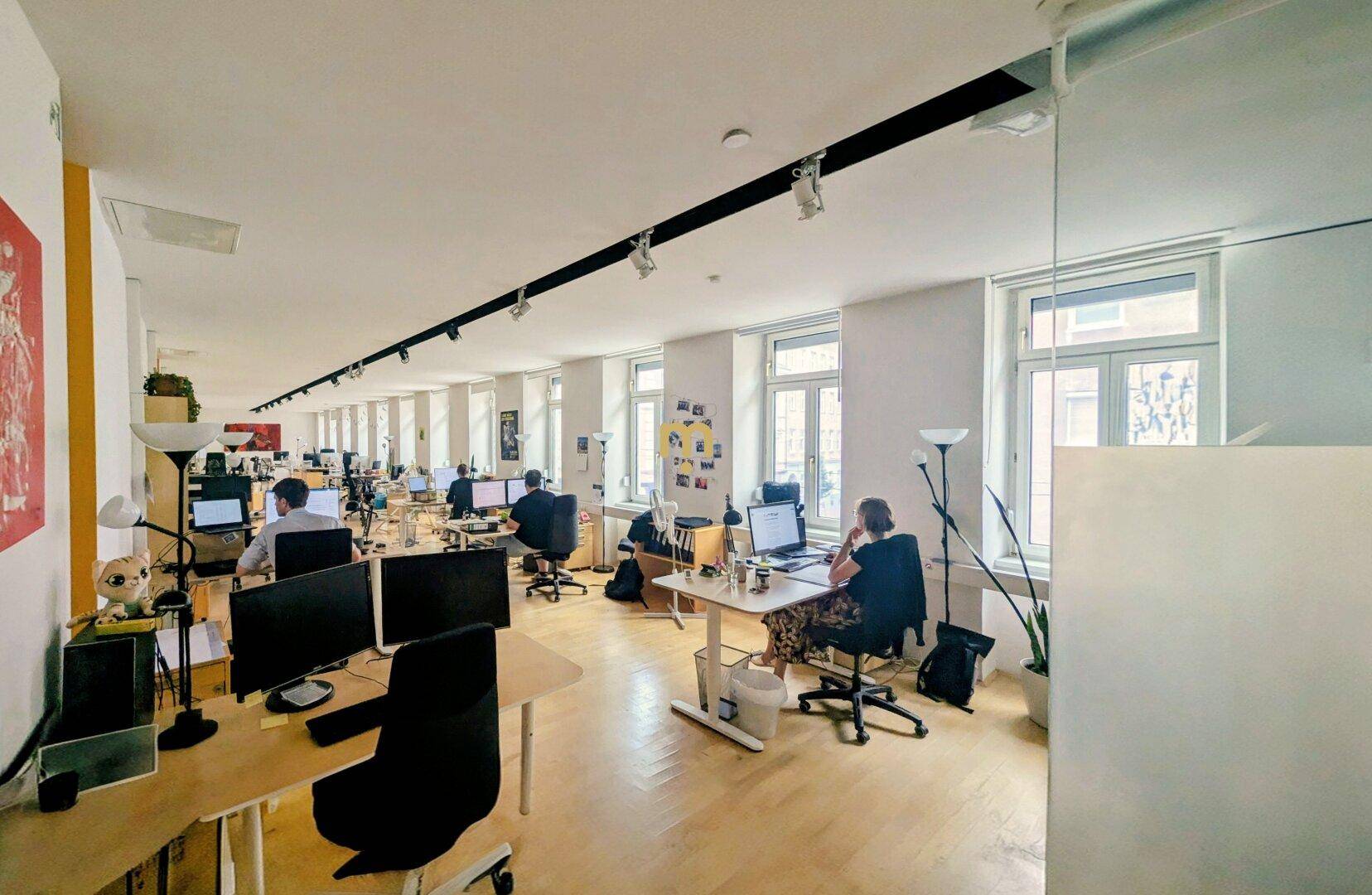 Großes Großraumbüro mit vielen Arbeitsplätzen, Holzfußboden und viel Tageslicht.