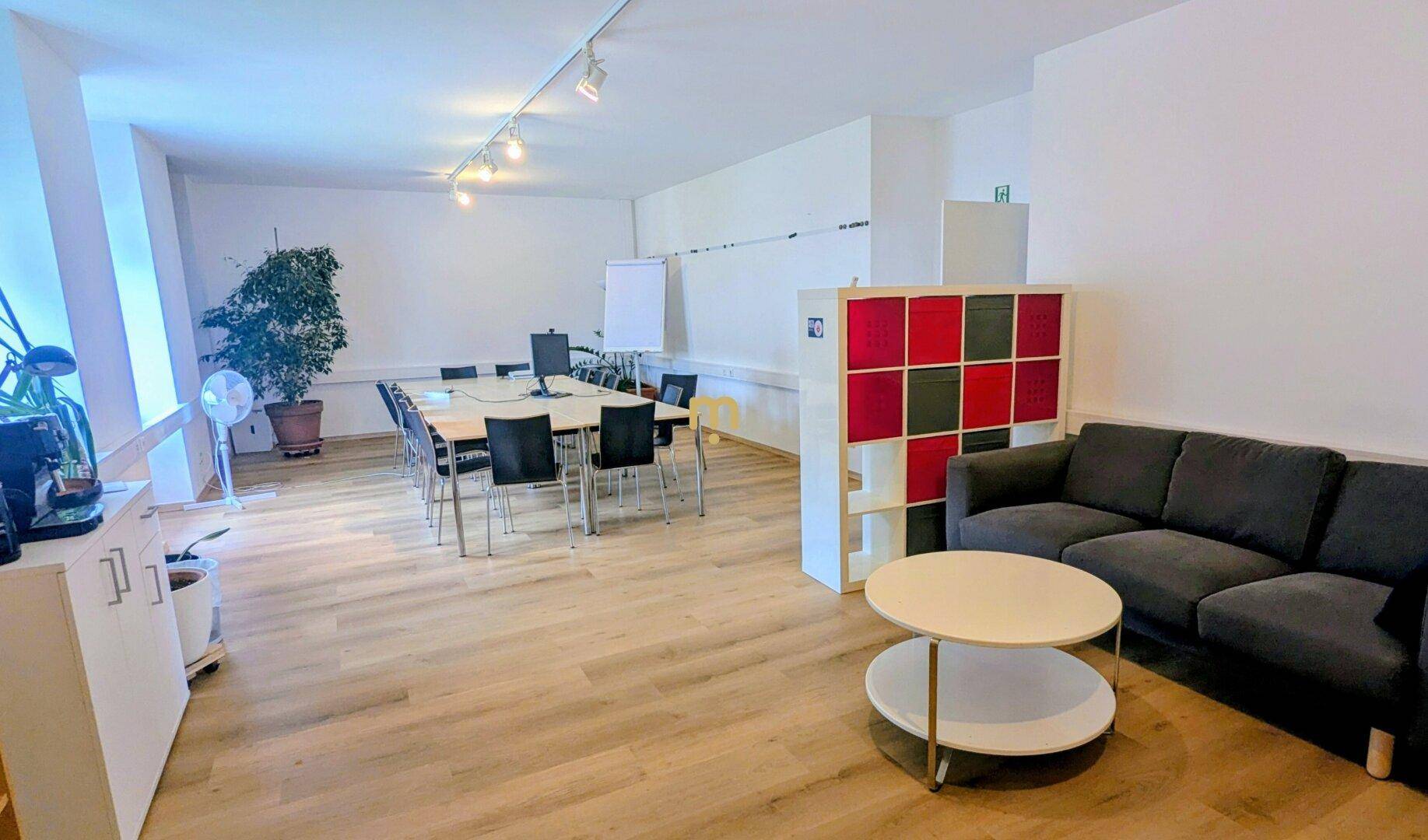Vielseitiger Büroraum mit Besprechungstisch, Sofa und Regalsystem.