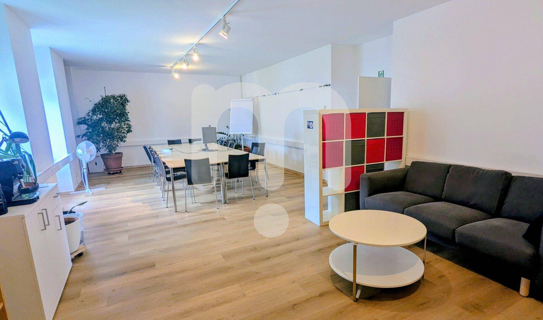 Flexibler Büroraum mit Besprechungstisch, Sofa, Couchtisch und einem Regal, ideal für Pausen oder informelle Treffen.
