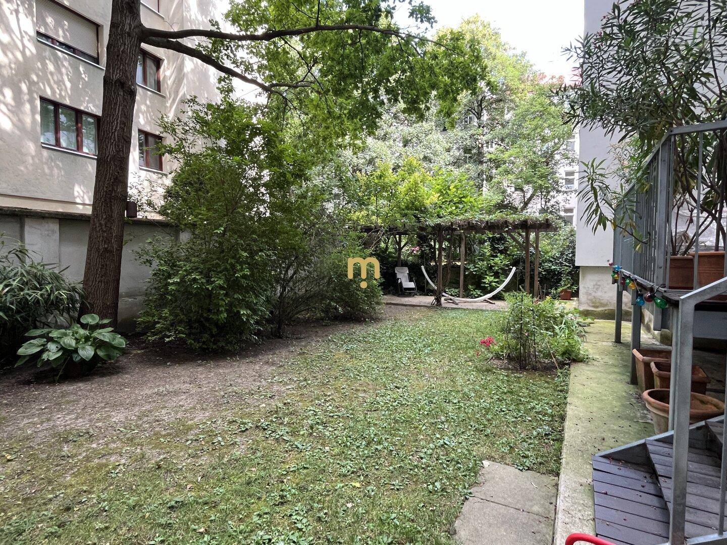 Grüner Gemeinschaftsgarten mit Bäumen, Rasenfläche und einer Hängematte zum Entspannen.