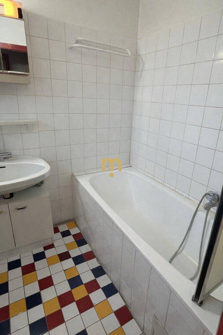 Badezimmer mit Badewanne, Waschbecken und einem auffälligen, farbigen Fliesenboden.