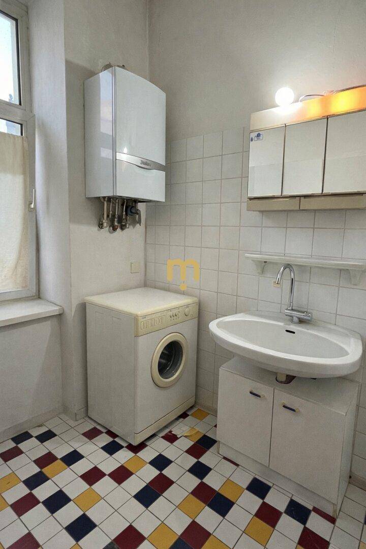Raum mit Waschmaschine, Boiler, Waschbecken und farbigem Fliesenboden.