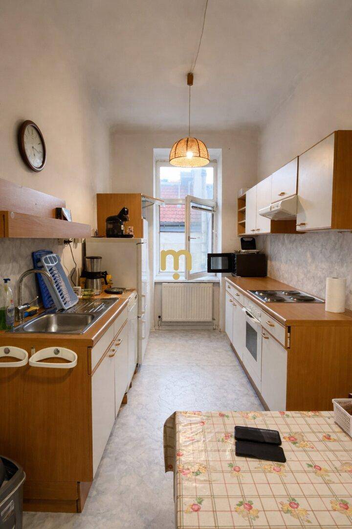 Funktionale Küche mit älteren Einbaumöbeln, Fenster und einem kleinen Esstisch.