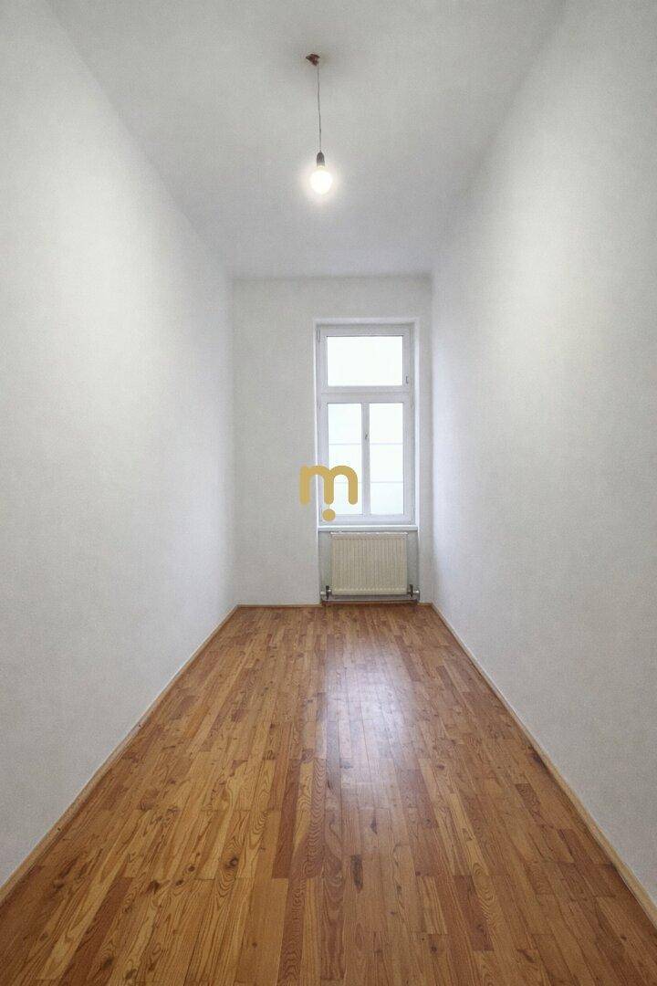 Schmaler Raum mit Holzboden und einem Fenster, ideal als Schlafzimmer oder Arbeitszimmer.