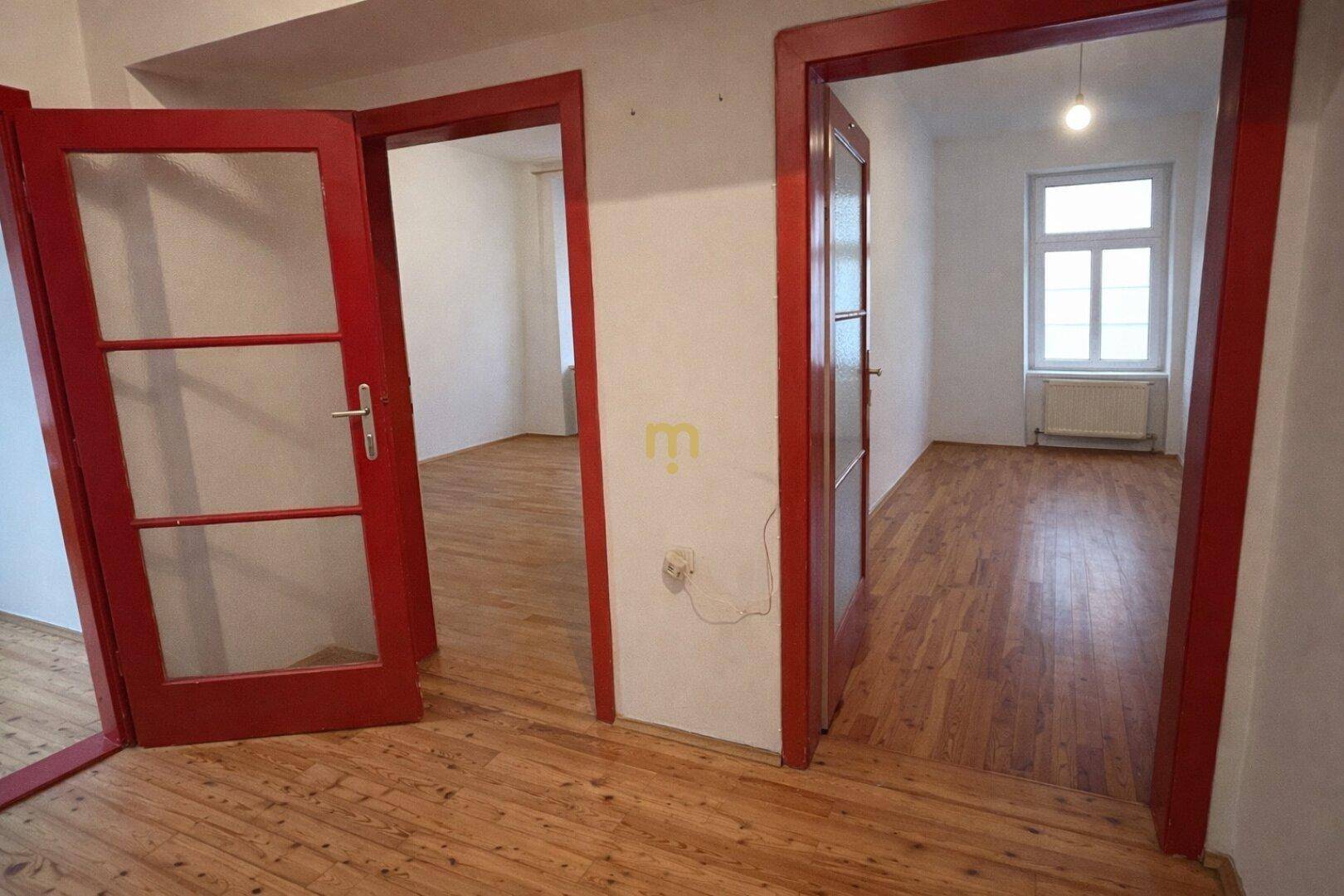Blick durch rote Türen in angrenzende, leere Zimmer mit Holzboden.