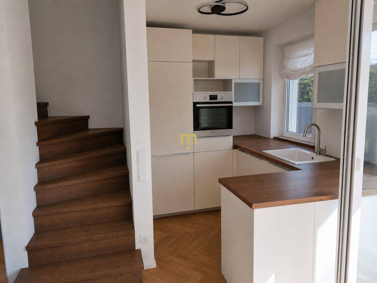 Moderne Einbauküche mit Holztheke und integriertem Backofen neben einer Holztreppe.