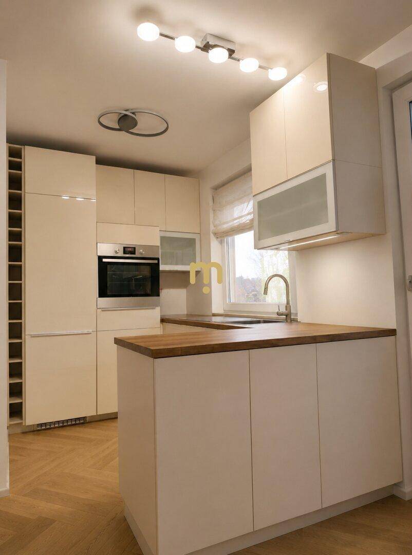 Helle, moderne Einbauküche mit glänzenden Fronten, Backofen und Fenster für Tageslicht.