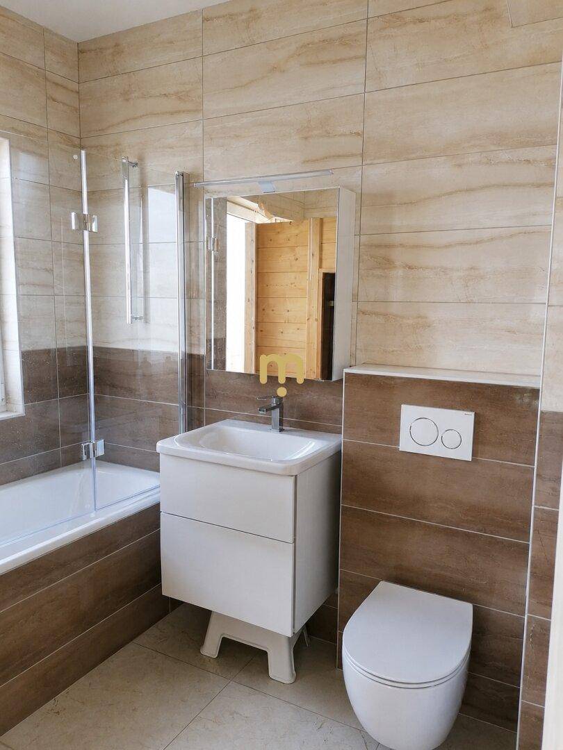 Modernes Badezimmer mit Badewanne, Waschbecken, WC und hellbraunen Fliesen an Wänden und Boden.