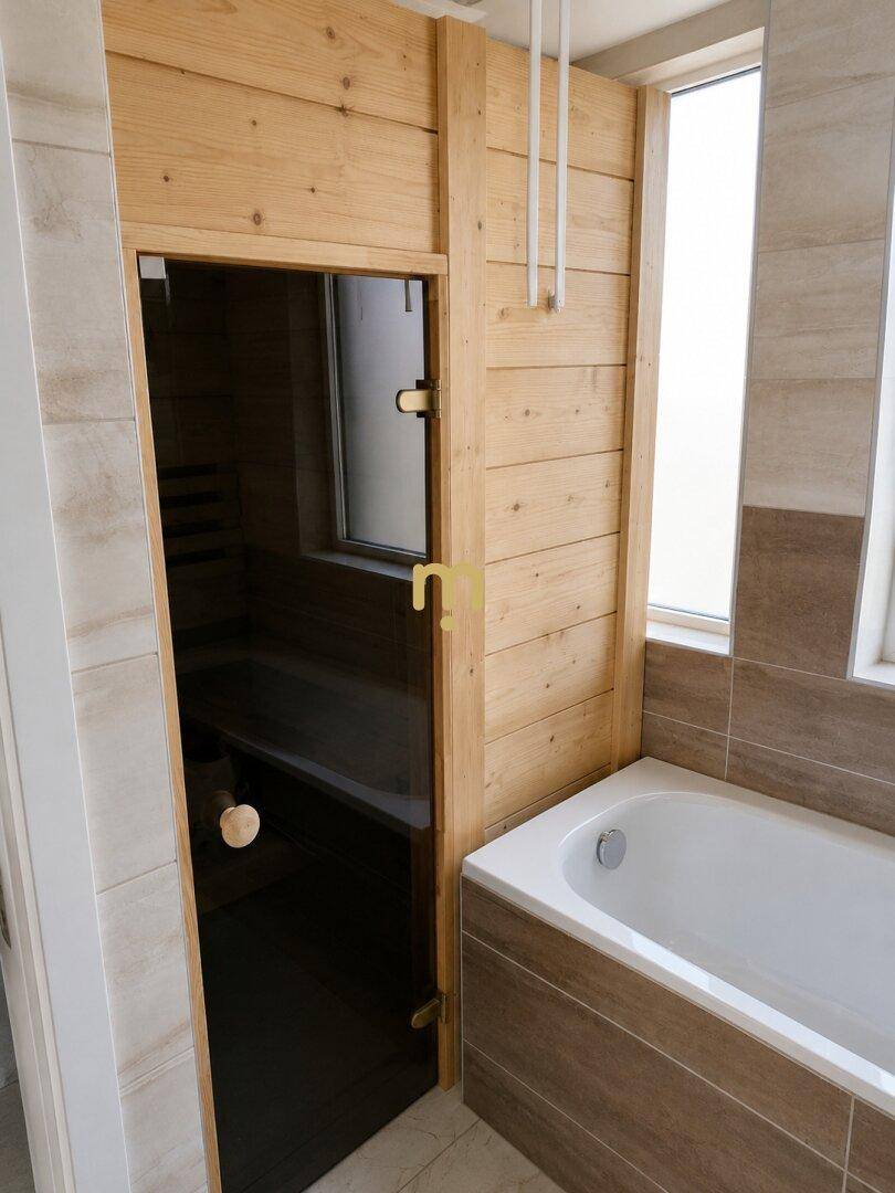 Badezimmer mit Badewanne und integrierter Sauna, umgeben von hellen Fliesen und Holzverkleidung.
