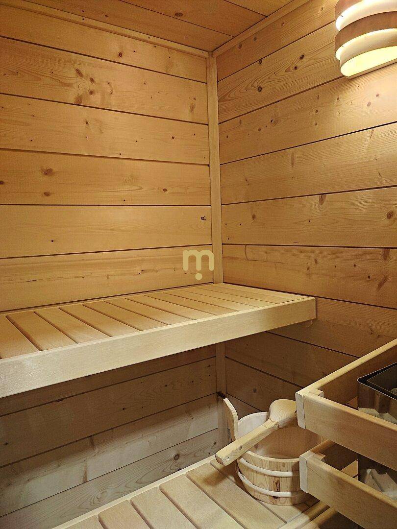 Innenansicht einer holzverkleideten Sauna mit Bänken und traditionellem Zubehör für Entspannung.