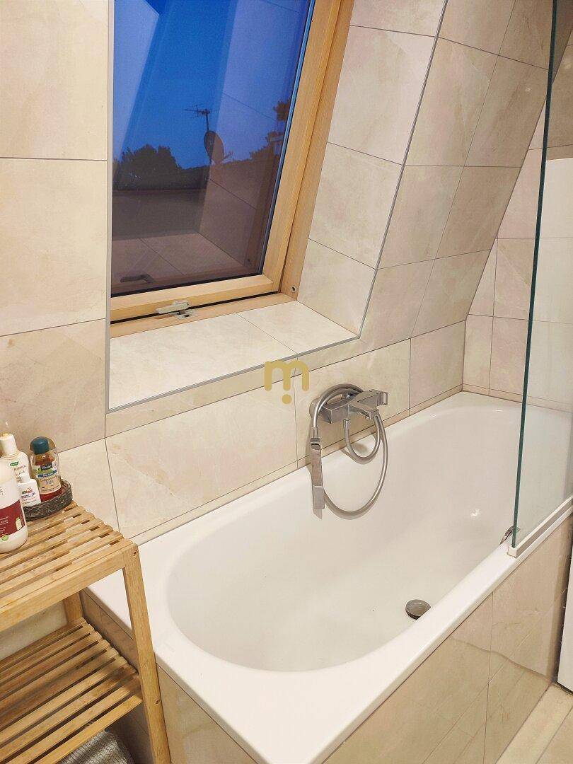 Badezimmer mit Badewanne unter einem Dachfenster und hellen Fliesen an Wänden und Boden.
