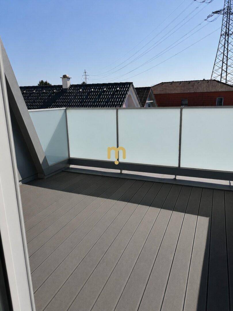 Moderner Balkon mit Holzboden und Milchglasgeländer unter blauem Himmel mit Fernblick.