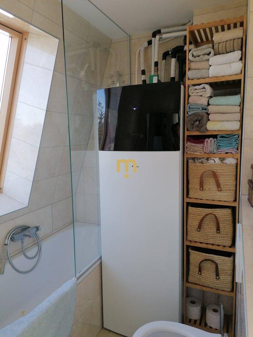 Badezimmer mit Badewanne, Wärmepumpe und praktischem Holzregal für Handtücher.