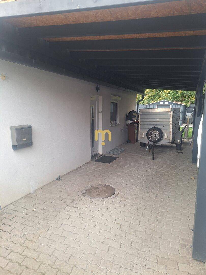 Überdachter Eingangsbereich und gepflasterte Zufahrt mit Carport neben dem Haus.