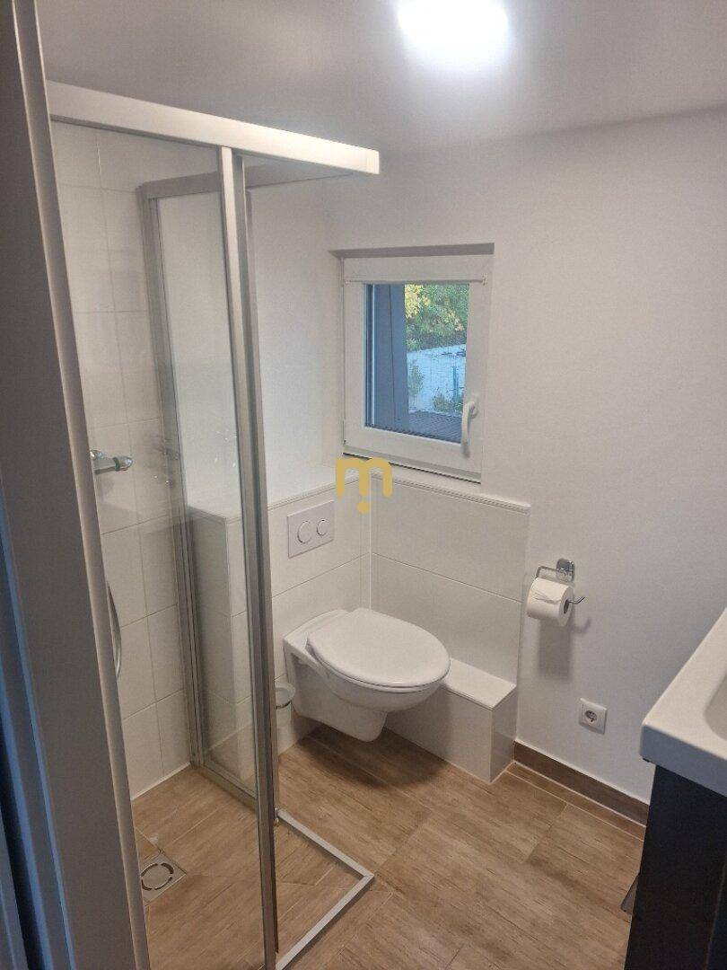 Modernes Badezimmer mit Duschkabine, wandhängendem WC und Fenster für Tageslicht.
