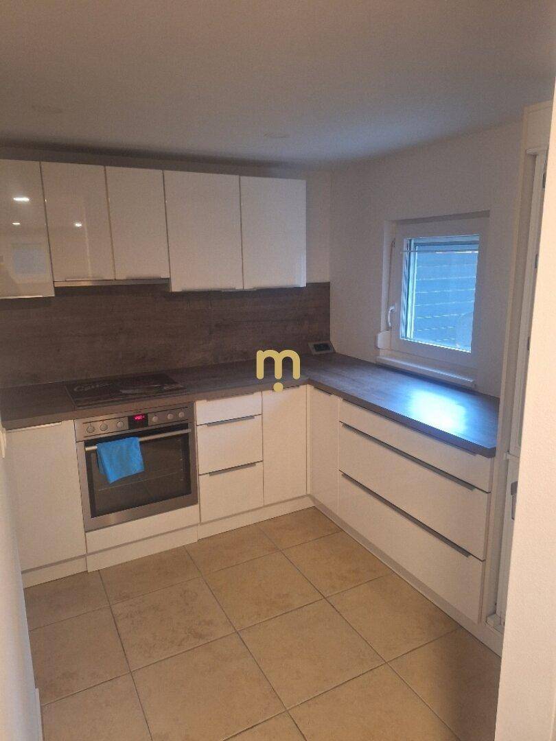 Moderne Küche mit weißen Hochglanzschränken, dunkler Arbeitsplatte und Fliesenboden.