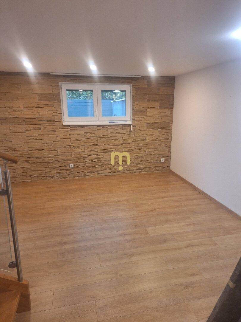 Heller Wohnraum mit Laminatboden, strukturierter Akzentwand und Fenster.