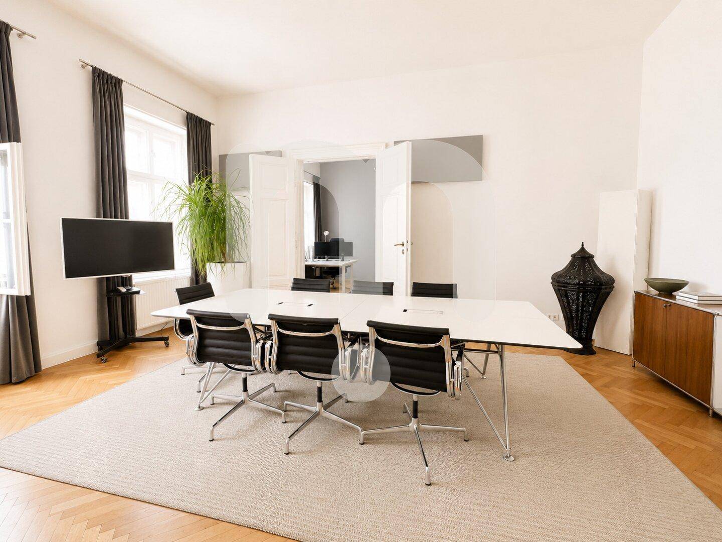 Moderner Konferenzraum mit großem Tisch, bequemen Stühlen und einem Wandfernseher für Präsentationen.