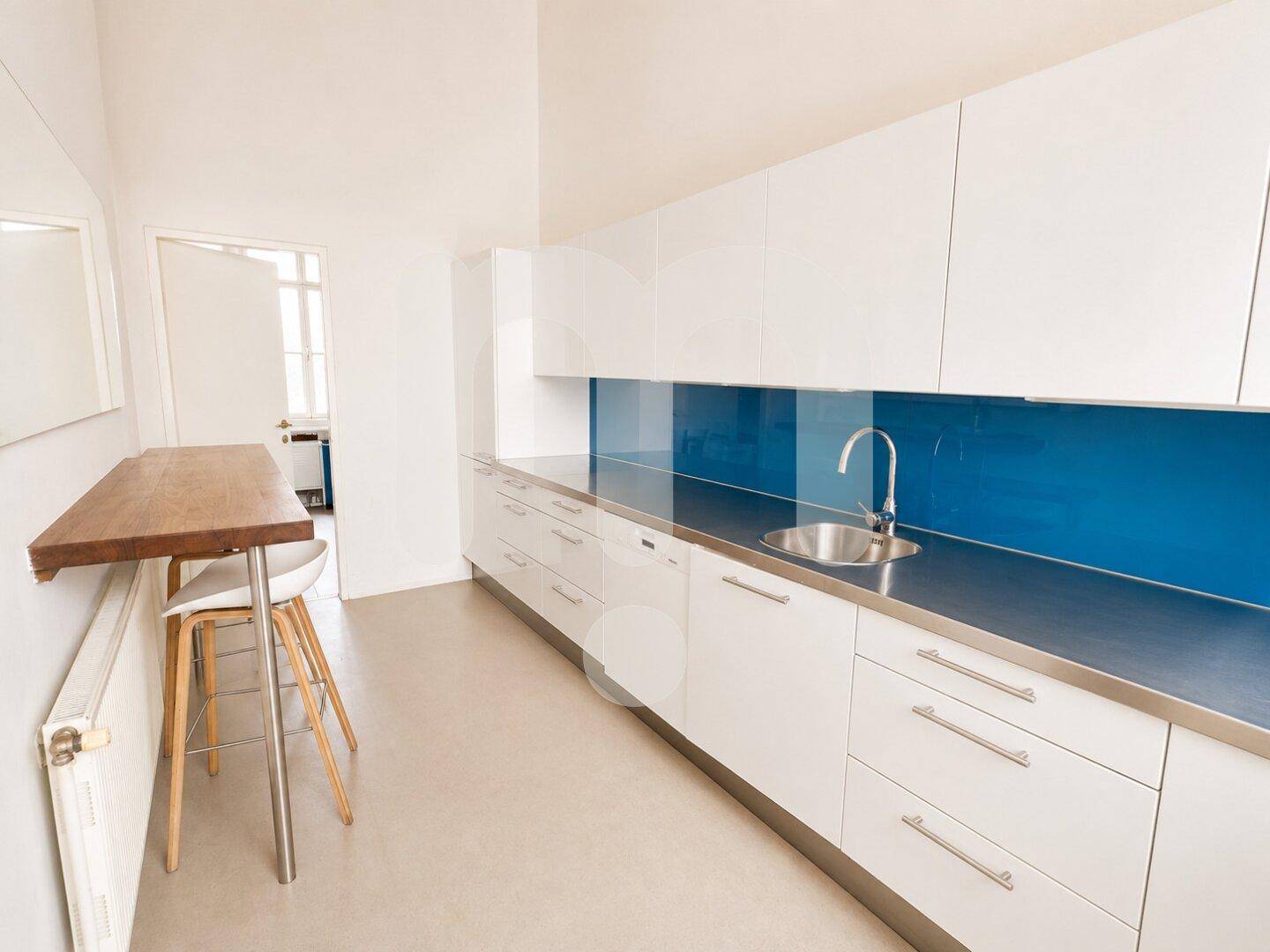 Moderne Küchenzeile mit weißen Hochglanzschränken, blauer Rückwand und Edelstahlspüle, inklusive Bartisch.