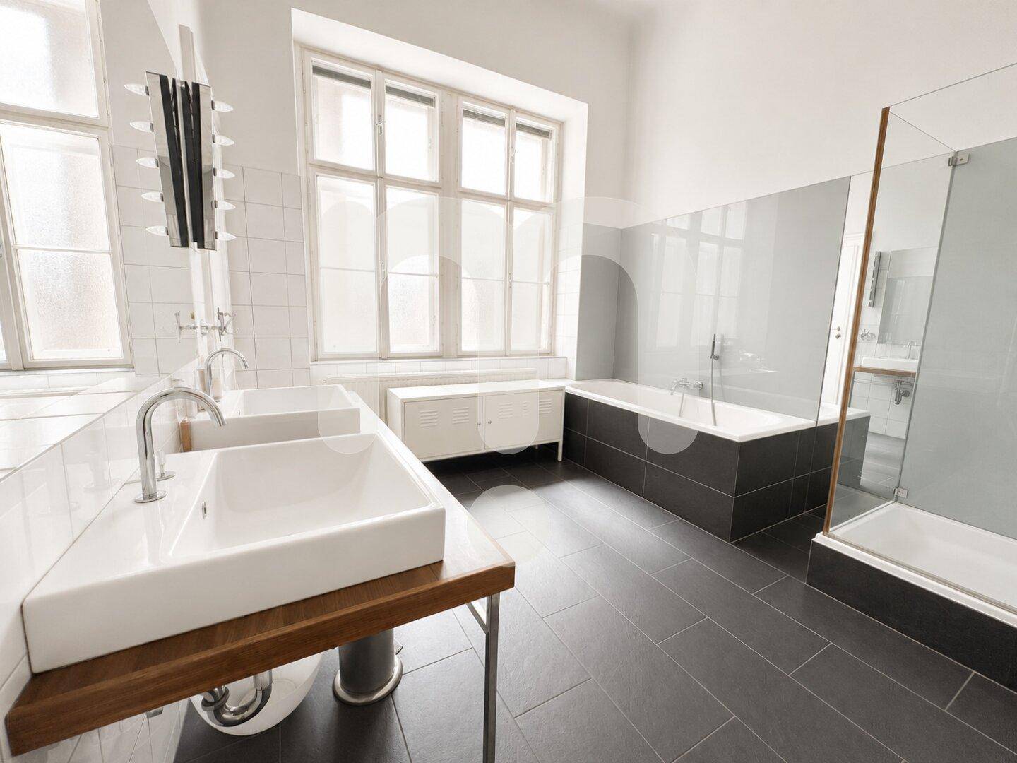Geräumiges Badezimmer mit zwei Waschbecken, Badewanne, begehbarer Dusche und großen Fenstern.