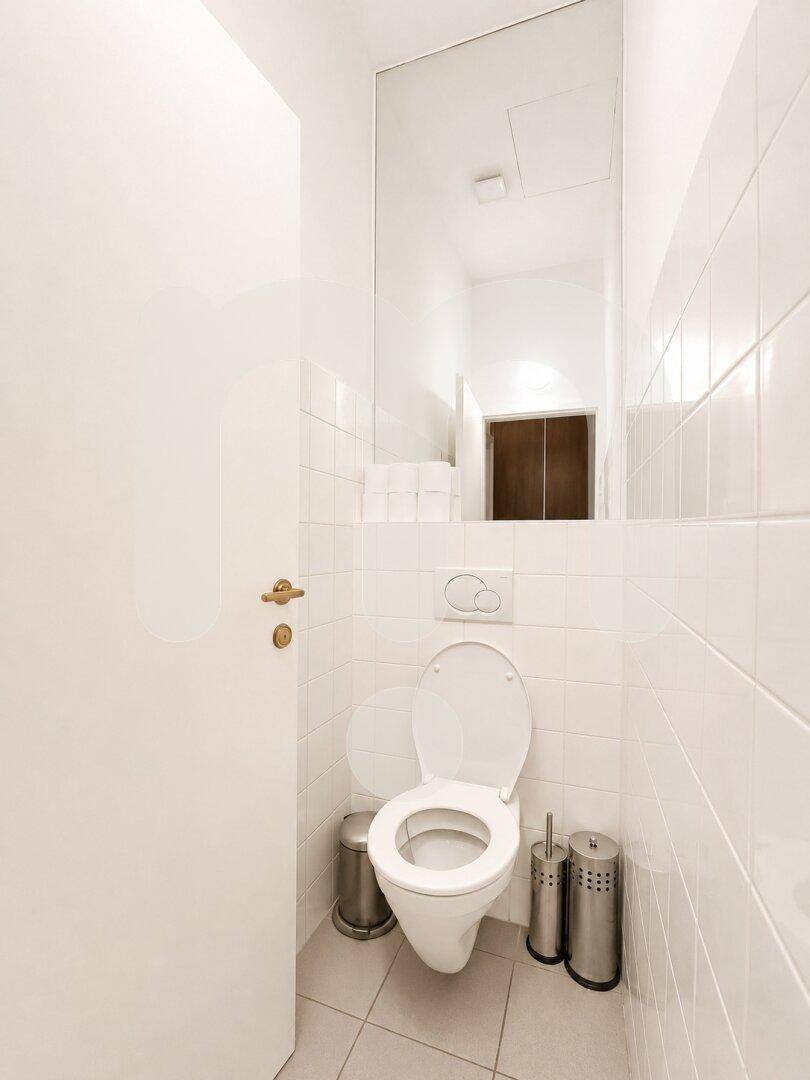 Kleines, hell gefliestes Gäste-WC mit wandhängender Toilette und großem Spiegel.