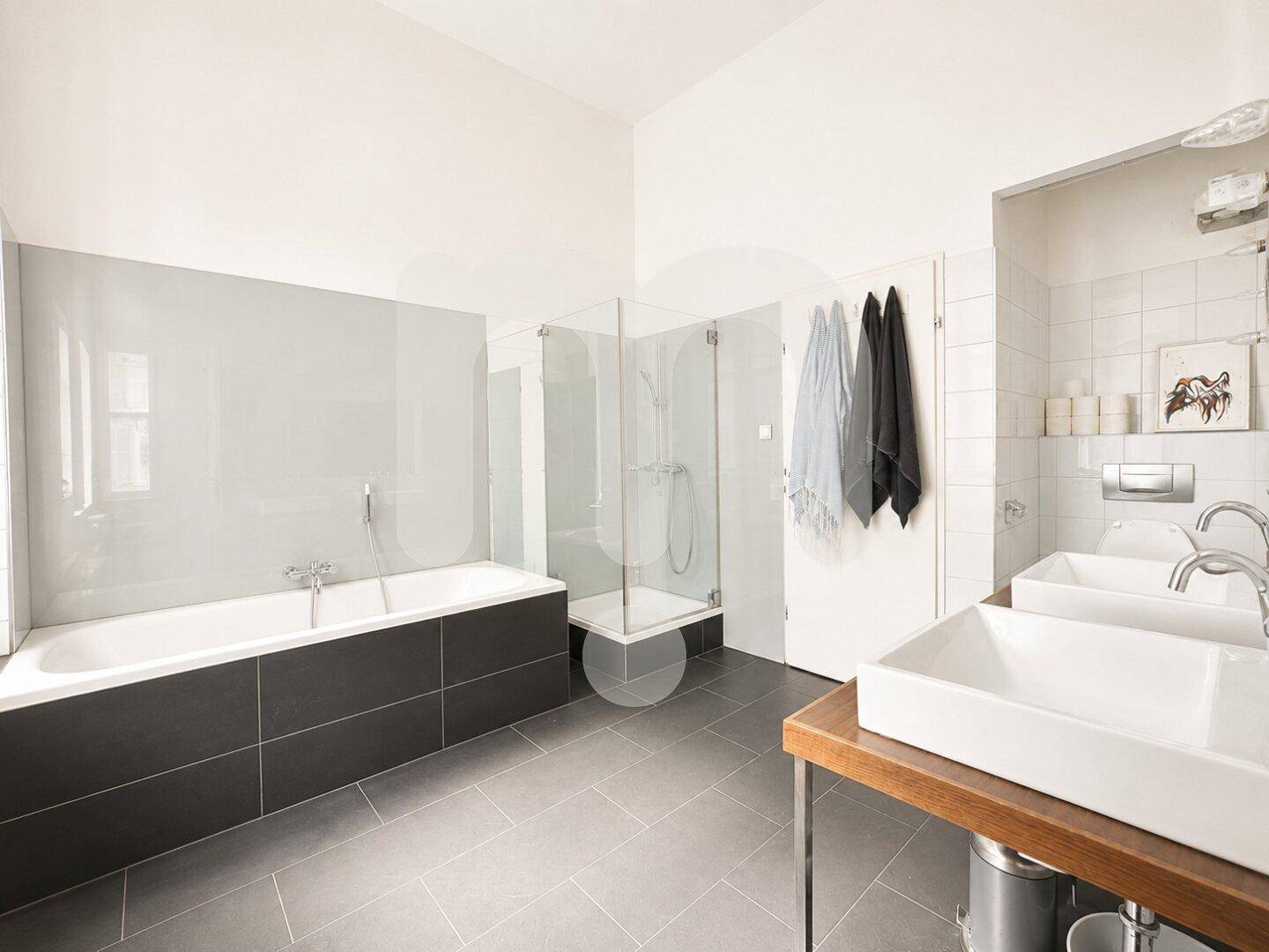 Modernes Badezimmer mit Badewanne, begehbarer Glasdusche und zwei Waschbecken, in hellen Farben gehalten.