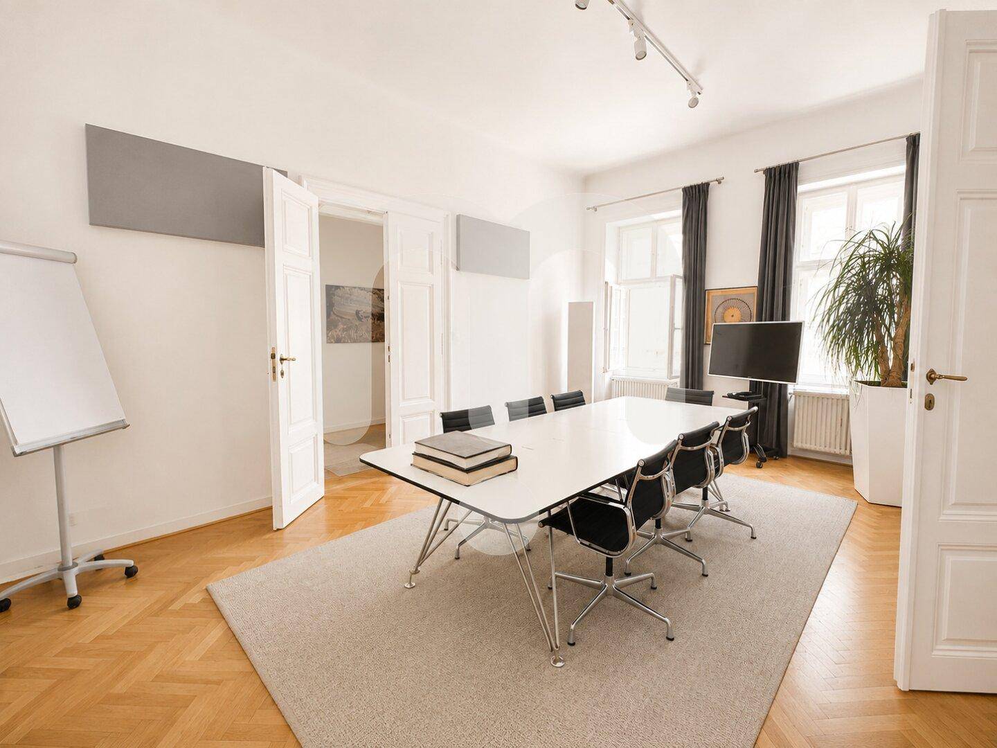 Konferenzraum mit großem Tisch, bequemen Stühlen, einem Whiteboard und Blick in einen weiteren Raum.
