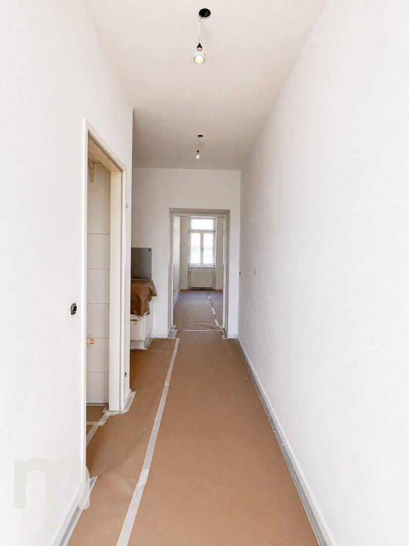 Langer, heller Flur mit Blick in ein weiteres Zimmer, Boden für die Endverlegung vorbereitet.