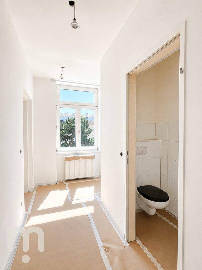 Heller Flur mit Zugang zu einem WC und Tageslicht durch ein Fenster, Boden vorbereitet.