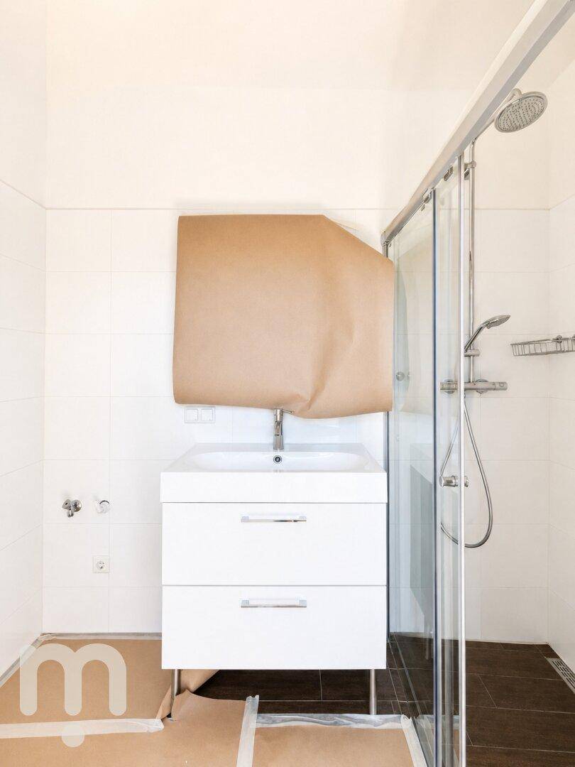 Modernes Badezimmer mit Duschkabine und Waschtisch, teilweise abgedeckt für Renovierungsarbeiten.