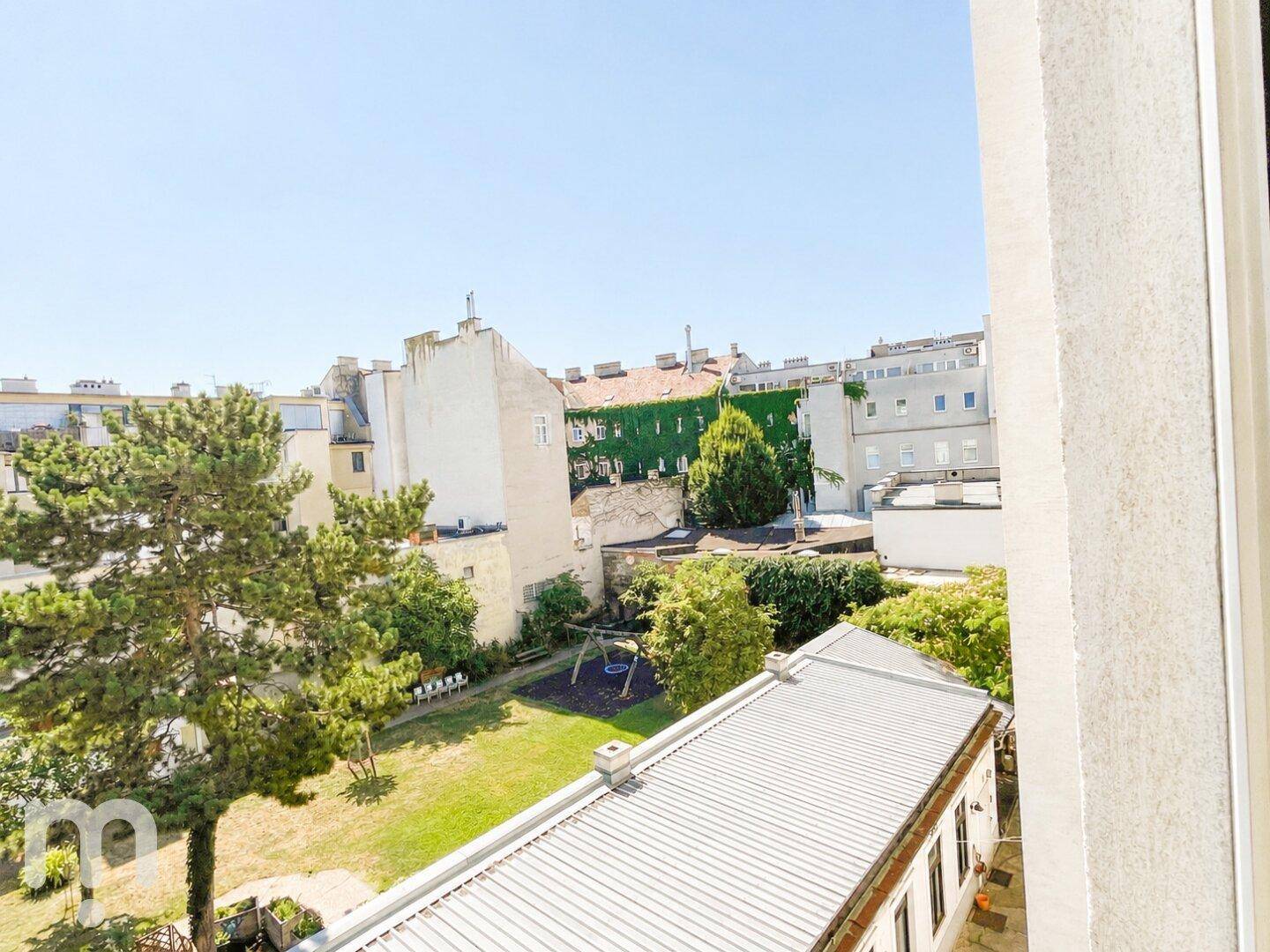 Blick aus dem Fenster auf einen grünen Innenhof mit Spielplatz und Bäumen.
