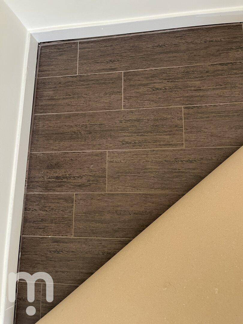 Nahaufnahme eines dunkelbraunen Fliesenbodens, teilweise abgedeckt für Renovierungsarbeiten.