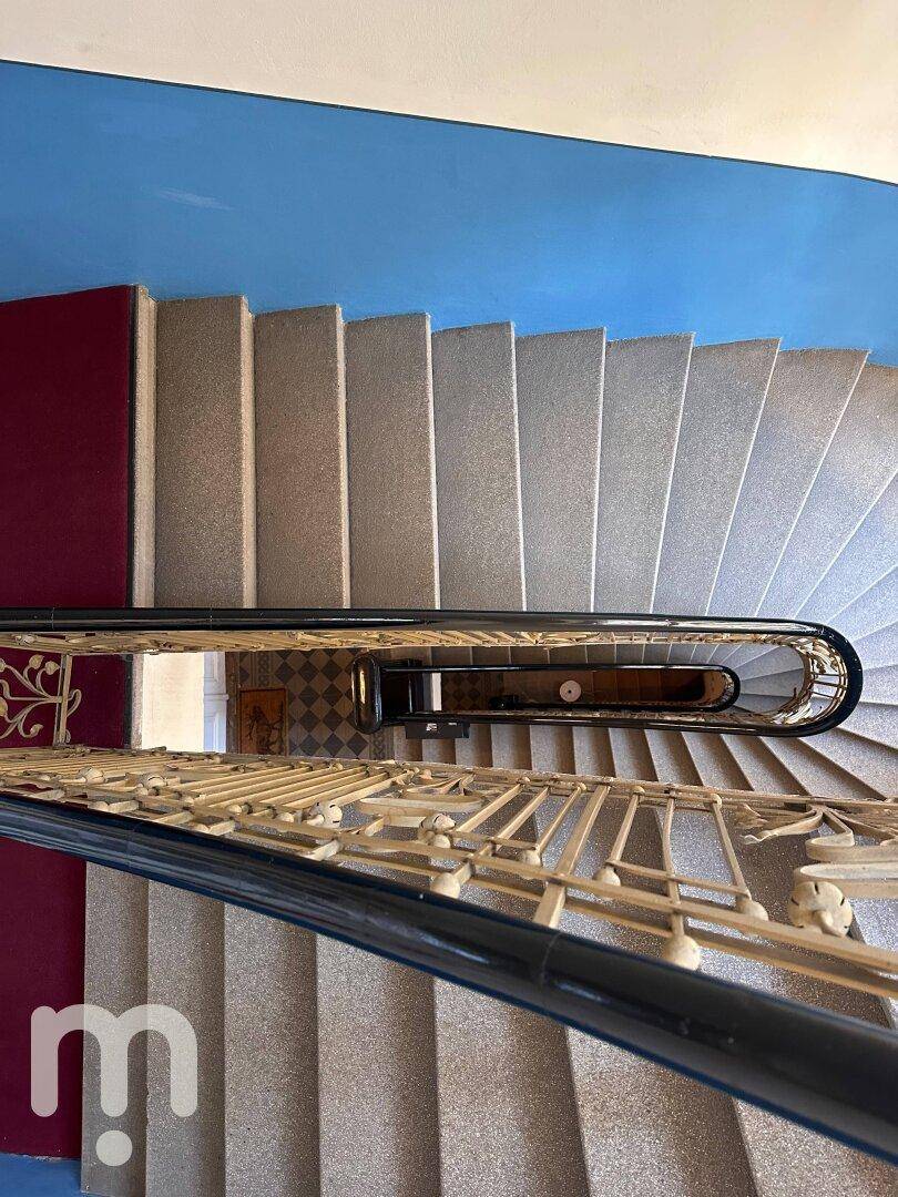 Eine elegante Wendeltreppe mit schmiedeeisernem Geländer und blauen Wänden in einem historischen Gebäude.