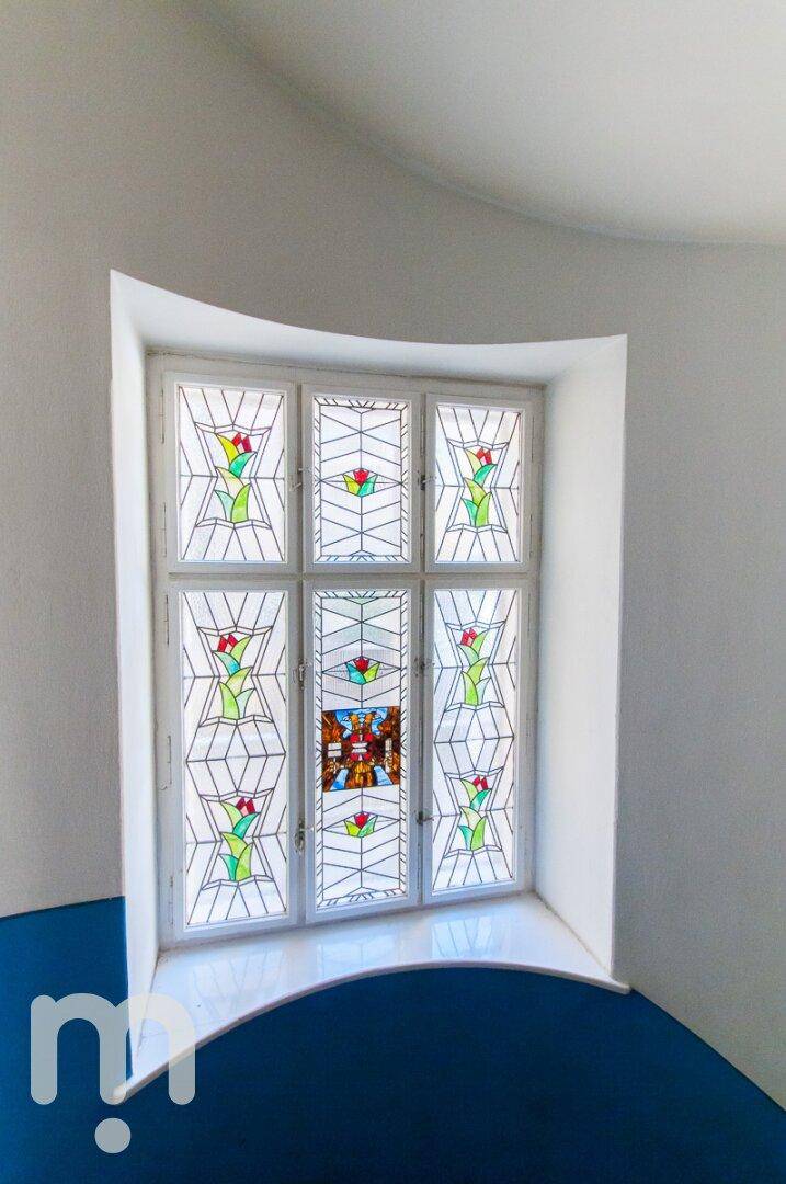 Ein farbenfrohes Buntglasfenster mit floralen Mustern in einem historischen Gebäude.