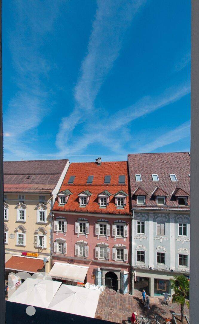 Blick aus dem Fenster auf historische Gebäude mit roten Dächern und blauem Himmel.