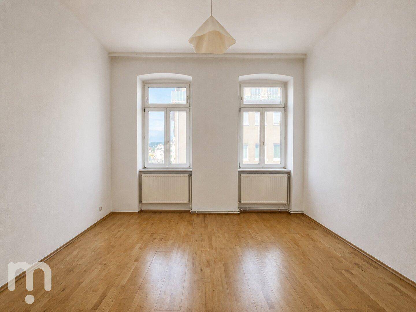 Geräumiges, leeres Zimmer mit Parkettboden und zwei großen Fenstern, bereit zur individuellen Gestaltung.